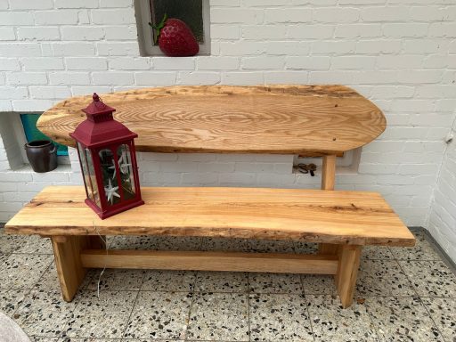 Holzbank mit natürlicher Maserung und roter Laterne auf der Sitzfläche.